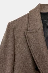 Abrigo largo de corte recto confeccionado en mezcla de lana, con cuello de solapa, cierre frontal cruzado con botones y bolsillos laterales.