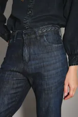 Jean de corte acampanado estilo setentero, confeccionado en denim azul oscuro. Presenta una cintura con detalle de trenzado integrado y un calce ajustado en la parte superior que se ensancha desde la rodilla hacia abajo.