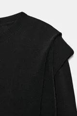 Jersey negro de punto, manga larga, con cuello redondo y detalle de pliegues o volados en la zona de los hombros.