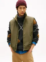 Chaleco verde militar Tommy Hilfiger de cuello alto, con cierre frontal de cremallera y dos bolsillos laterales de ojal. Presenta un diseño sin mangas con logo monotipo bordado en el pecho.