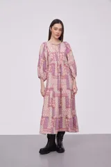 Vestido midi de viscosa con estampado patchwork en tonos rosados y violetas. Presenta cuello redondo con cordones ajustables, mangas 3/4 abullonadas y diseño holgado con falda de volados.