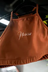 Top deportivo marrón con cuello halter y logo Hermod estampado en blanco.
