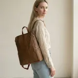 Mochila urbana de diseño rectangular, confeccionada en cuero sintético color marrón. Presenta un compartimento principal con cierre, manija superior y correas ajustables para llevar en la espalda.
