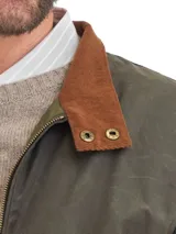 Campera de algodón encerado en color verde oliva, con cierre frontal, puños y ruedo elásticos, y cuello de pana en color marrón con detalle de broches metálicos.