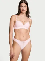 Panty tipo tanga de tiro bajo color rosado, confeccionado en microfibra suave con detalles de encaje y roseta decorativa en la parte frontal.