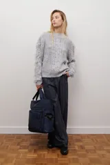 Buzo de punto color beige con cuello redondo, mangas largas con flecos decorativos y diseño de trenzas en el frente.