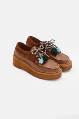 Zapato tipo mocasín de plataforma color bordó, confeccionado en una combinación de cuero liso y gamuza. Presenta cordones bicolores con detalle de borlas decorativas en el empeine.