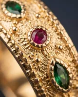Anillo de bronce con baño de oro y textura granulada, adornado con piedras incrustadas en tonos verdes y rojos.