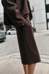 Bermuda de tiro alto en color marrón chocolate, con diseño de corte recto y largo por encima de la rodilla. Presenta pinzas delanteras, bolsillos laterales y cierre frontal con cremallera, botón y gancho.