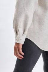 Sobrecamisa de paño en color beige, con cuello camisero, cierre frontal de botones y dos bolsillos delanteros con solapa. Presenta un corte holgado y mangas largas.