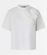 Blusa boxy de manga corta, confeccionada en algodón, con cuello redondo y detalles de flores de tejido aplicadas en el hombro y sisa.