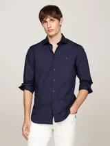 Camisa de manga larga para hombre, color azul marino, de corte slim fit, confeccionada en popelina con tecnología flex que incluye algodón orgánico. Presenta cuello con botones y el logo de Tommy Hilfiger bordado en el pecho.