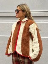 Campera de corderito con diseño de rayas verticales en colores marrón y crema, con cierre frontal y detalles de ribete en color rojo.