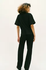Camiseta de algodón compacto color negro, con cuello redondo, manga corta y detalle de aplique metálico en el frente que genera un ligero fruncido lateral.