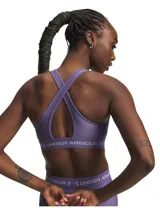 Top deportivo Under Armour de soporte medio, color violeta, con diseño de espalda cruzada y banda elástica inferior con logo de la marca. Confeccionado en tejido HeatGear de doble capa, de secado rápido y alta transpirabilidad.