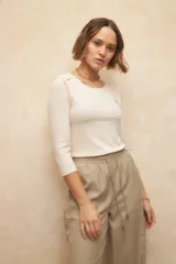 Remera color crema de manga tres cuartos, cuello redondo y costuras marcadas en los hombros. De un textil elastizado, súper cómoda y ceñida al cuerpo.