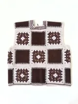 Chaleco sin mangas, confeccionado con cuadrados de cuero negro perforado combinados con cuadrados de crochet en hilo de algodón negro y blanco, con detalles centrales en rojo.