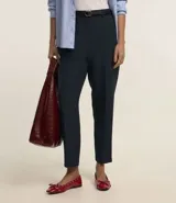 Pantalón de sastrería corte carrot, color beige, con cintura alta, pinzas frontales y cinturón fino incorporado con hebilla metálica.