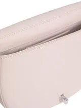 Cartera cruzada Calvin Klein de color rosa pálido, con forma de media luna o silla de montar. Presenta un logo metálico plateado con las iniciales 'CK' en el frente. La correa es ajustable y delgada.