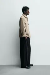 Sobrecamisa relaxed fit color beige con tejido elástico, cuello solapa, manga larga con puños abotonados, bolsillos de plastrón con solapa en el pecho, bolsillos laterales de vivo en la cadera y cierre frontal de botones.
