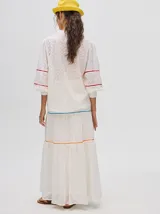 Falda larga blanca confeccionada en broderie de algodón con diseño de paneles escalonados, detalles de galones con transparencias en color azul y naranja, y pretina elástica con cordón ajustable.
