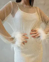 Vestido corto de red con acabado brillante, manga larga y detalle de plumas blancas en los puños. Presenta un diseño ajustado con escote redondo.