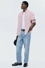 Camisa de sarga de algodón de corte relajado, con estampado a cuadros en tonos rosados y blancos, cuello americano, manga larga con puños abotonados y un bolsillo frontal en el pecho.