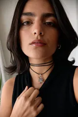 Collar con dije de acero quirúrgico en forma de flor de lirio, montado sobre un tiento de cuero encerado largo.