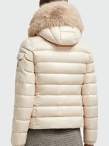 Campera puffer color crema de Moncler, modelo Badyf, con relleno de plumas, cierre frontal con cremallera, bolsillos laterales con cremallera y capucha con borde de piel sintética.