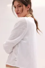 Blusa blanca de lino con escote en V y mangas largas con puños elásticos, combinando delantera estructurada de lino y espalda de algodón con spandex.