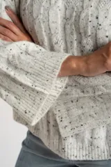 Sweater de punto con textura de ochos, color gris melange con motas oscuras, cuello redondo y mangas largas con terminación acampanada.