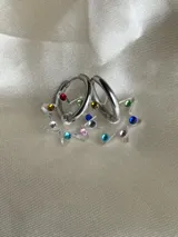 Aros tipo argolla dorada con dije colgante en forma de estrella de acrílico color rosa.