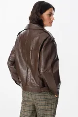 Chaqueta de cuero sintético con textura granulada, corte oversize, cuello camisero, cierre frontal con botones a presión, bolsillos frontales tipo cargo y detalles de charreteras en los hombros.