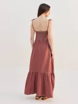Vestido largo de algodón denim con diseño de rayas verticales en color azul marino y beige. Cuenta con tirantes finos ajustables con lazos en los hombros, escote recto y corte suelto con un volante en el bajo.
