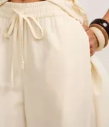 Pantalón pantalona color beige, confeccionado en viscolino con elástico y lazo ajustable en la cintura, de corte amplio y fluido.