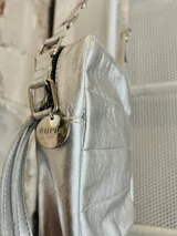 Mini bandolera de cuero color plata con diseño frontal capitoneado. Cuenta con cierre superior, correa larga regulable y diseño combinado de cintas y detalles metálicos.