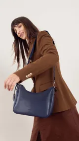 Bandolera de cuero sintético color marrón, con cierre trasero y división interna. Incluye correa de galón ajustable y un pequeño charm colgante.