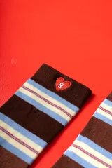 Par de medias de caña media con diseño de rayas horizontales en tonos marrón, celeste y crema. Presentan un detalle bordado de un corazón rojo con la letra R en el puño de una de las medias.