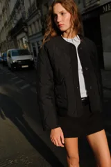 Chaqueta acolchada de cuello redondo y manga larga, con cierre frontal de botones y dos bolsillos delanteros de plastrón. Presenta un diseño de costuras en forma de rombos.