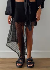 Falda corta negra de encaje con diseño irregular y un volante largo asimétrico en un lateral. Posee cintura elástica y forro interior.