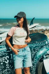 Top corto color crema con mangas cortas color rosa y estampado de palmeras y texto en el frente.