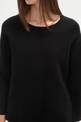 Sweater negro liso, holgado, con cuello a la base y broches decorativos en el lateral.