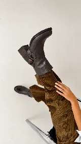 Botas de caña baja en cuero color marrón oscuro, con taco cuadrado y punta redondeada. Presentan un diseño tipo western con estribo desmontable que incluye una hebilla metálica decorativa.