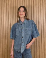 Sobrecamisa de denim soft azul, con cuello clásico, mangas cortas amplias, bolsillos frontales con solapa y cierre de botones metálicos.