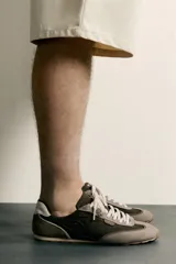 Zapatillas de estilo retro con cordones blancos, capellada marrón combinada con paneles de gamuza gris y detalles en cuero. Suela de goma a contraste.