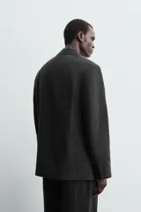 Blazer negra de corte relajado confeccionada en tejido con mezcla de lyocell. Tiene cuello con solapas de muesca, manga larga con puños abotonados, bolsillos de doble vivo en la cadera, bolsillo interior y cierre frontal cruzado con botones.