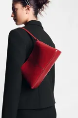 Bolso de hombro en formato mini color rojo, con detalle de pespuntes centrales y asa ajustable. Cuenta con compartimento interior con cremallera y doble compartimento exterior con cierre imantado.