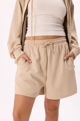Conjunto deportivo compuesto por un buzo con cierre frontal, capucha y bolsillos, y un short con cintura elástica y cordón ajustable. Confeccionado en tejido soft premium de color marrón.