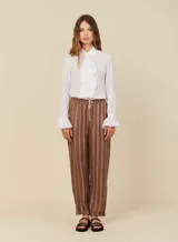 Pantalón babucha de lino a rayas verticales marrones y blancas, con cinturilla elástica con lazo para anudar y tres bolsillos funcionales.