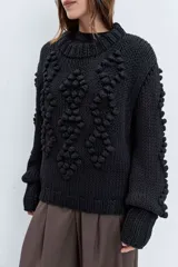 Sweater de punto grueso color rojo, con cuello alto y diseño de relieves tipo pompones en el frente y las mangas. Presenta puños y ruedo acanalados.
